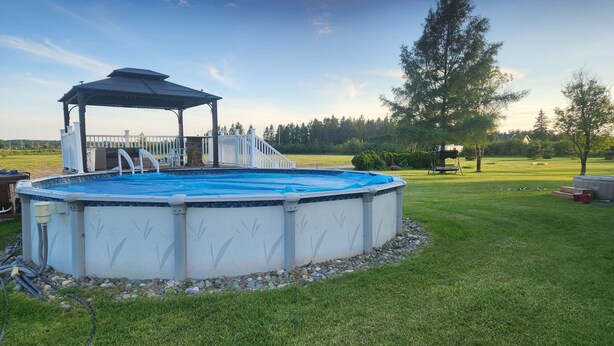An above-ground swimming pool with a covered deck area, surrounded by a well-maintained lawn and trees. - Unique getaway or travel stop, just 10 minutes off TransCan Highway (Grand Sudbury)