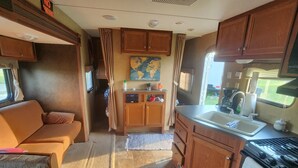 A compact RV interior with a kitchenette, a sofa, and a dining area. - Unique getaway or travel stop, just 10 minutes off TransCan Highway (Grand Sudbury)