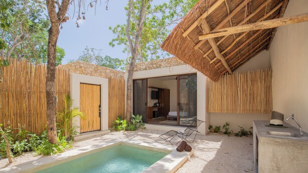 A pool area with a concrete edge, a wooden fence, and a thatched roof structure. - ZENDA TULUM LUXURY VILLAS (Tulum)