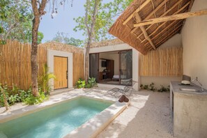 Uma área de piscina com borda de concreto, cerca de madeira e estrutura com telhado de palha.