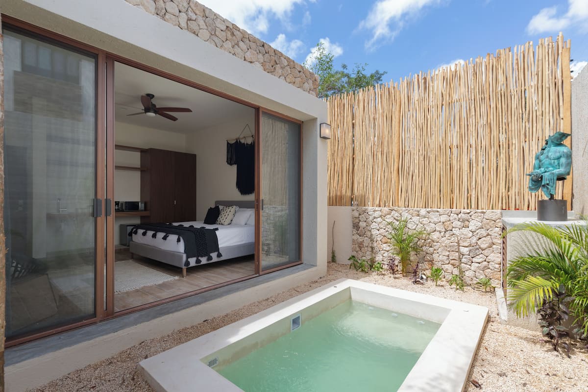 A modern bedroom with a large sliding glass door leading to a balcony, a small pool, and a stone wall with a bamboo fence.