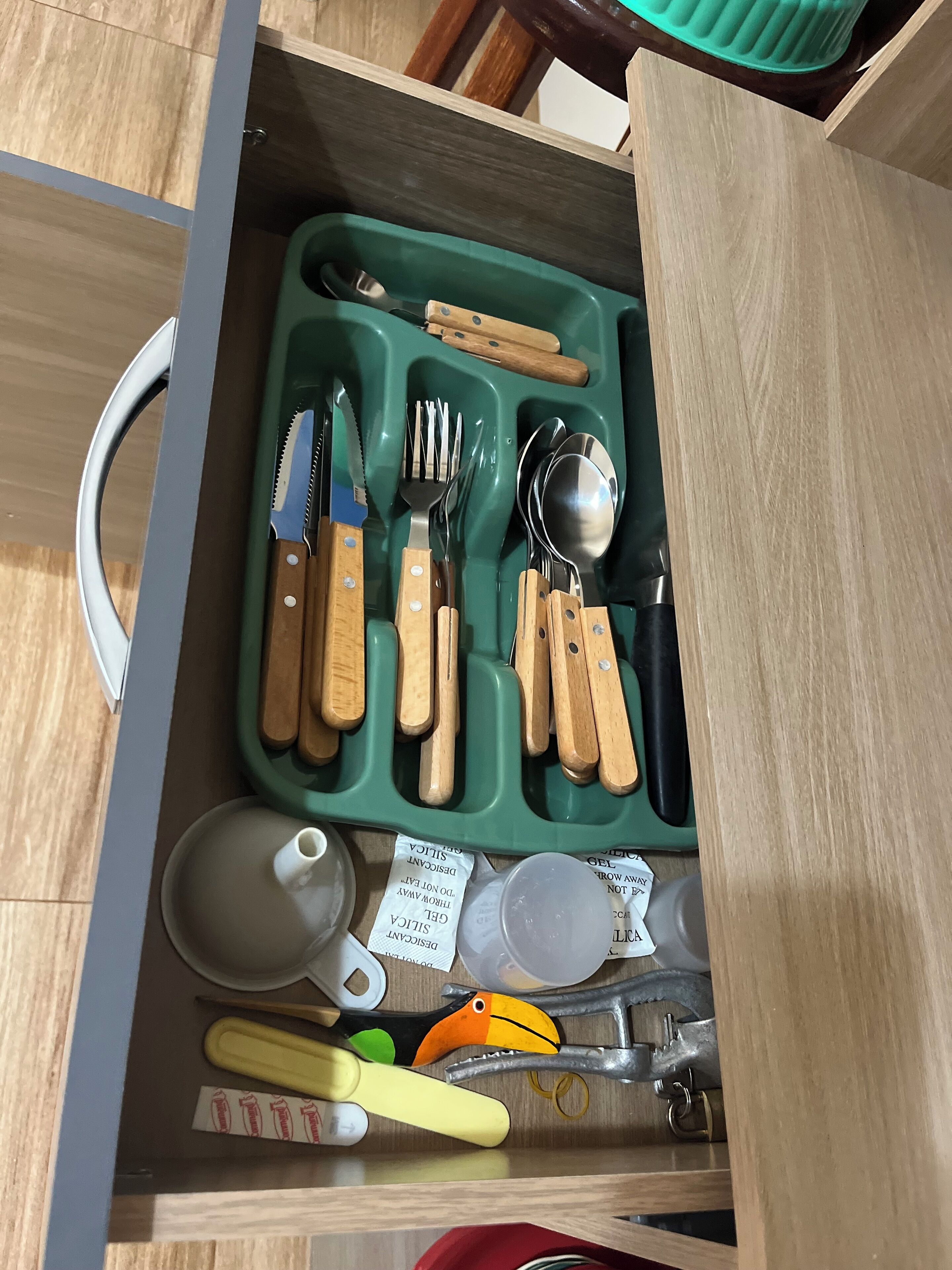A drawer with a green tray containing various kitchen utensils, including knives, a spoon, and a pair of scissors.