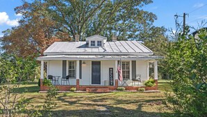 Una piccola casa bianca con un portico, un cartello di benvenuto e una bandiera americana.