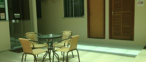 A small, enclosed dining area with a round table and four wicker chairs. There are two doors, one with a glass panel and another with a wooden shutter. A sign on the wall indicates smoking is prohibited.