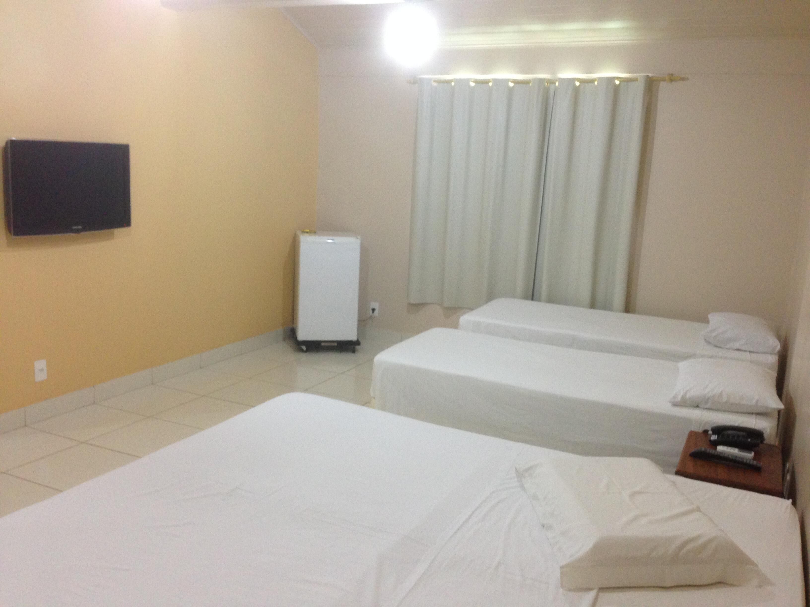 Habitación de hotel con dos camas, un televisor montado en la pared, un refrigerador y una cortina.