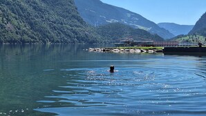 Un lago con una persona che nuota, circondato da montagne boscose e un molo con barche.