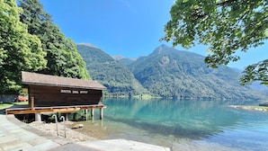 Un edificio in legno con la scritta "BAITA DAL SURF" fronteggia un lago limpido, sullo sfondo si vedono le montagne.