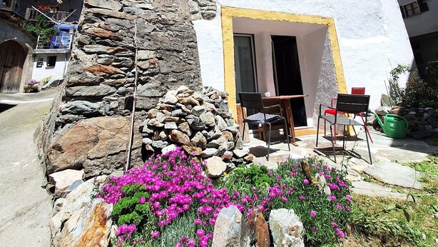 Un edificio bianco con una base in pietra, una finestra e una porta. All'esterno ci sono sedie e un tavolo.
