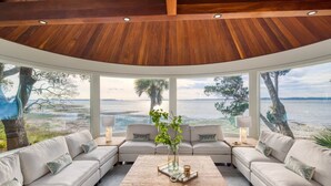 A modern interior with a curved ceiling, large windows offering a view of the water, and a seating area with a central coffee table.