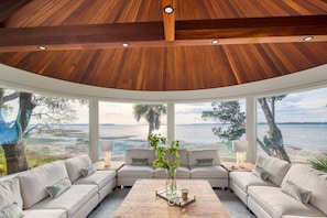 A modern interior with a curved ceiling, large windows offering a view of the water, and a seating area with a central coffee table.