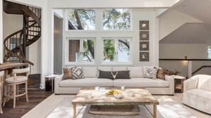 A spacious living room with a large window, a wooden staircase, and a cozy seating area.