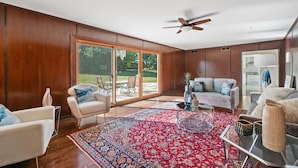 A spacious living room with a large window, a ceiling fan, and a red patterned rug. - Charming 4-bedroom house with WiFi, AC in upscale Oak Brook,near Oak brook mall (Oak Brook)
