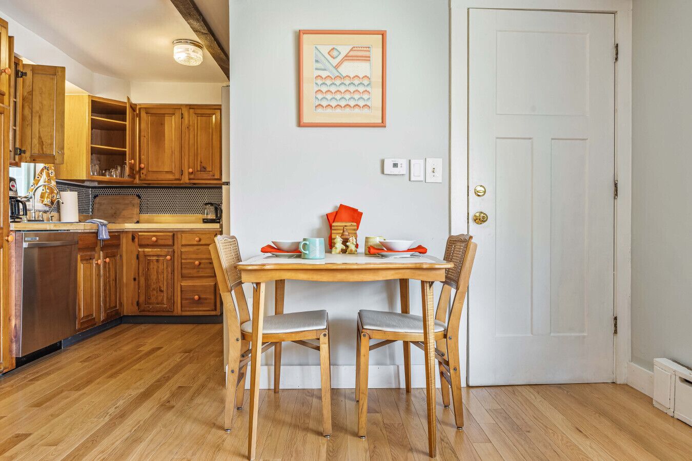 Eine Küche mit Holzausstattung, einem Esstisch mit Stühlen und einem gerahmten Bild an der Wand.