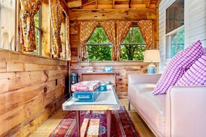 A cozy cabin interior with wooden walls, a sofa, a table with board games, and a window with curtains. - Poet's Nook: Cozy and Private 1BR Apartment (Scarborough)