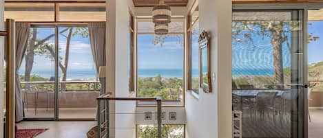 A spacious interior with a view of the ocean, a staircase, and a dining area with outdoor seating.
