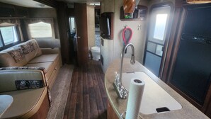 A compact RV interior with a kitchenette, a seating area, and a small bathroom.