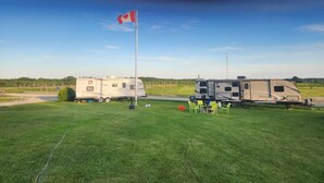 Two RVs parked on a grassy field with a flagpole in the center.