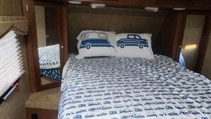 A compact bedroom with a bed, two pillows, a mirror, and a small seating area.