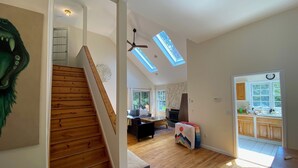 Un vaste espace de vie agrémenté d’un escalier en bois, d’une cheminée et d’un coin repas offrant une vue sur l’extérieur.