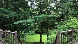 Une terrasse en bois, dotée d’une rambarde, qui mène à une zone herbeuse entourée d’arbres.