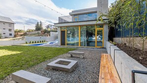 Een modern herenhuis met twee verdiepingen, een grote glazen deur, een zwembad en een verzorgde tuin met bankjes en een vuurkuil.