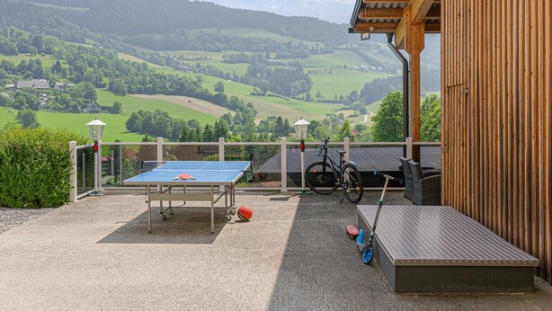 A ping pong table, bicycles, and a bench in an outdoor area with a view of green hills and houses. - Ferienwohnung Schöder (Schöder)
