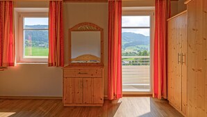 A room with wooden walls and ceiling, a wooden dresser with drawers, a mirror, and two windows with red curtains. - Ferienwohnung Schöder (Schöder)