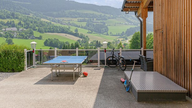 Eine Außenpatio mit Tischtennisplatte, Fahrrädern und einer kleinen Sitzecke mit Blick auf ein malerisches Tal.
