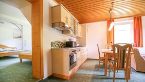 Eine kompakte Küche mit Holzausstattung, einer Mikrowelle und einem kleinen Backofen. Im angrenzenden Raum befindet sich ein Esstisch mit Stühlen und einer Bank.