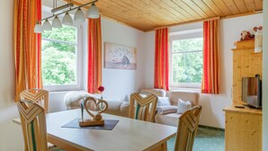 Ein gemütliches Zimmer mit Holztisch, Stühlen, einer Couch und einem Fernseher.