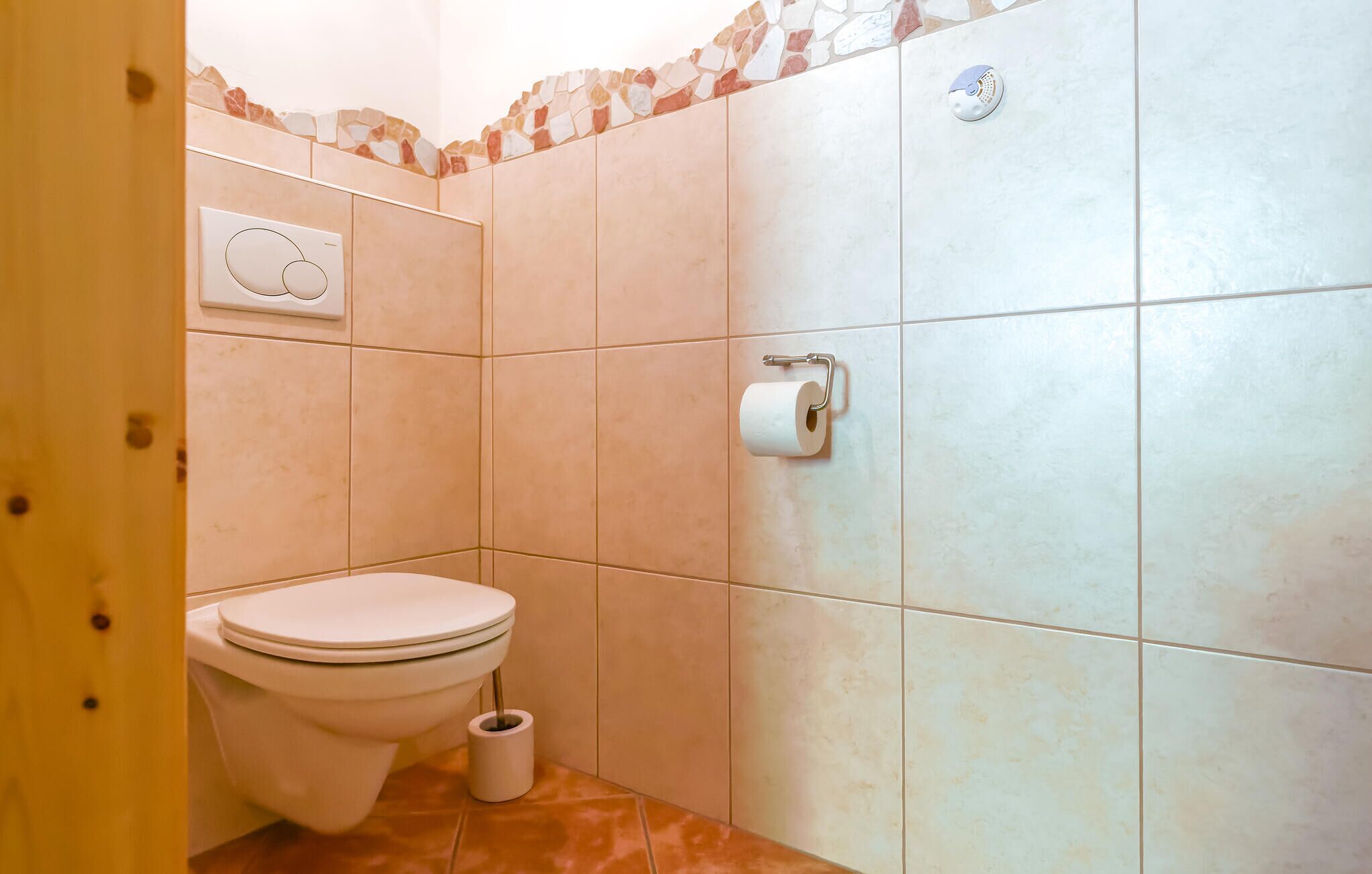 A small bathroom with a toilet, a toilet paper holder, and a wall-mounted flush button.