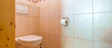 A small bathroom with a toilet, a toilet paper holder, and a wall-mounted flush button.