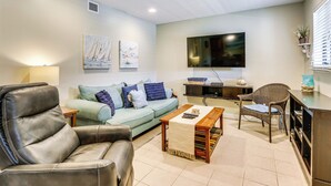 A modern living room with a leather sofa, a light green couch, a wooden coffee table, and a wicker chair. A flat-screen TV is mounted on the wall, and there is a small table with a lamp. - Private Beach Access: Hilton Head Island Condo! (Hilton Head Island)