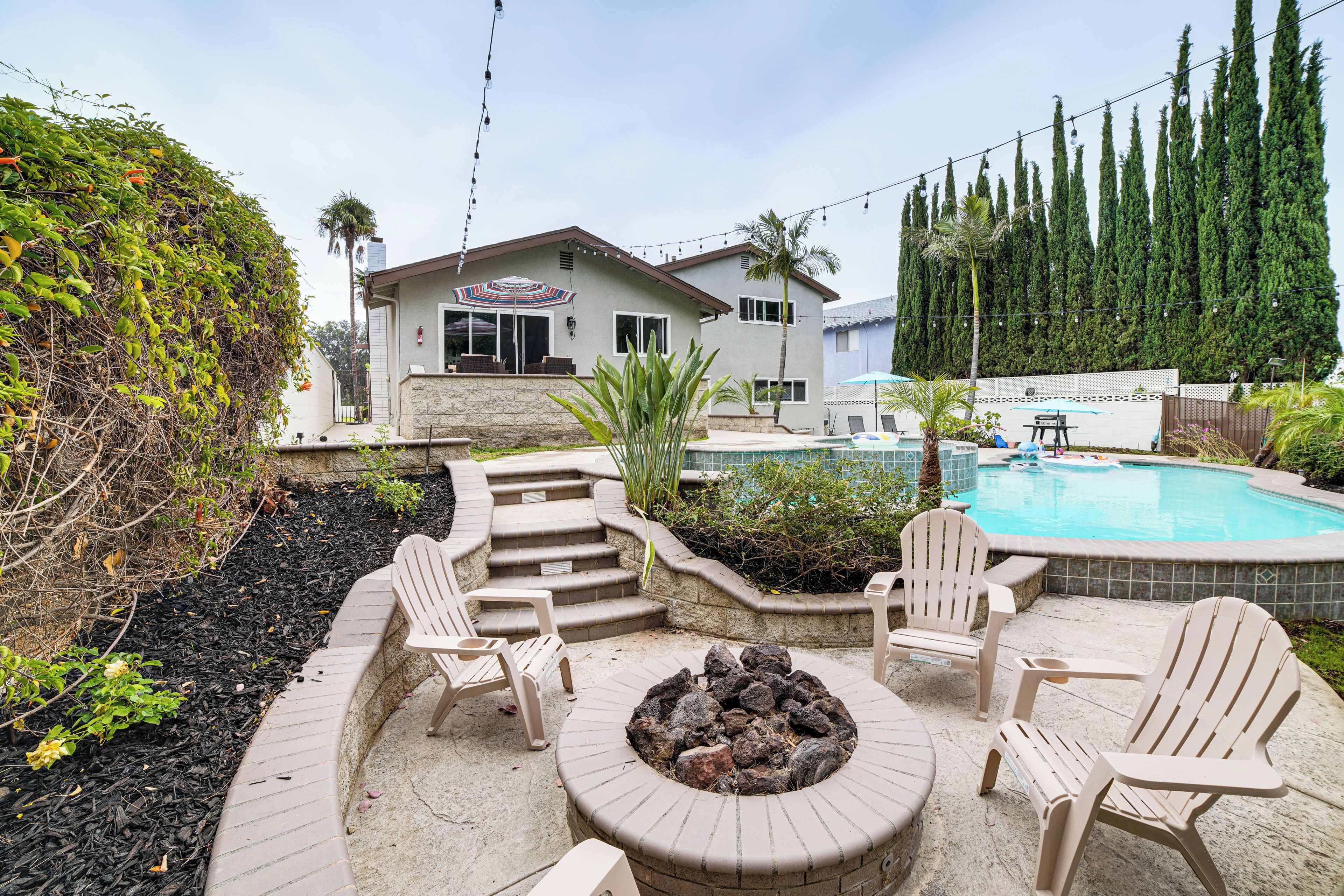 Ein Garten mit Feuerstelle, Sitzgelegenheiten im Freien, einem Swimmingpool und einem Haus im Hintergrund.