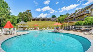 A large outdoor swimming pool with lounge chairs and umbrellas, surrounded by a fence and a building with balconies. - Hike, Golf & Swim: Blue Ridge Cabin Escape (Clayton)