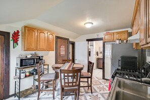 A compact kitchen with wooden cabinets, a microwave, a stove, and a dining area with chairs and a table. - 6 Mi to Boston Common: Apt in Medford! (Medford)