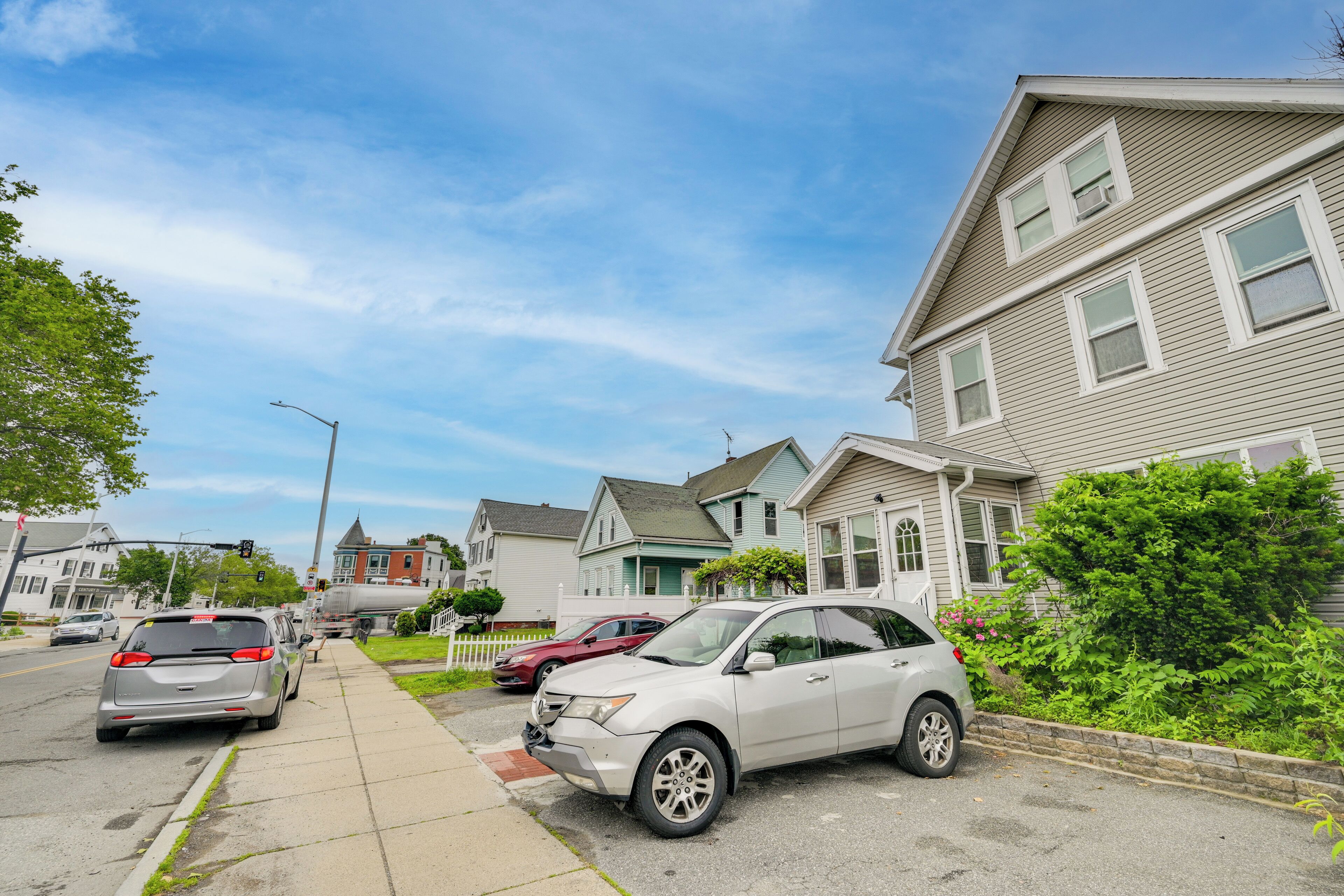 A residential street with houses, parked cars, and a clear sky.