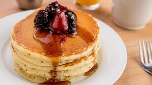 Une pile de crêpes nappées de sirop et garnies de fruits rouges, le tout présenté sur une assiette blanche.