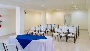 Une salle de conférence avec des rangées de chaises blanches et une table recouverte d’une nappe bleue.
