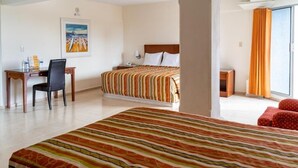 Une chambre d’hôtel avec un grand lit, un bureau avec une chaise, une petite table et une fenêtre avec des rideaux.