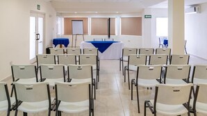 Une salle de conférence avec des rangées de chaises blanches et une table recouverte d’une nappe bleue.