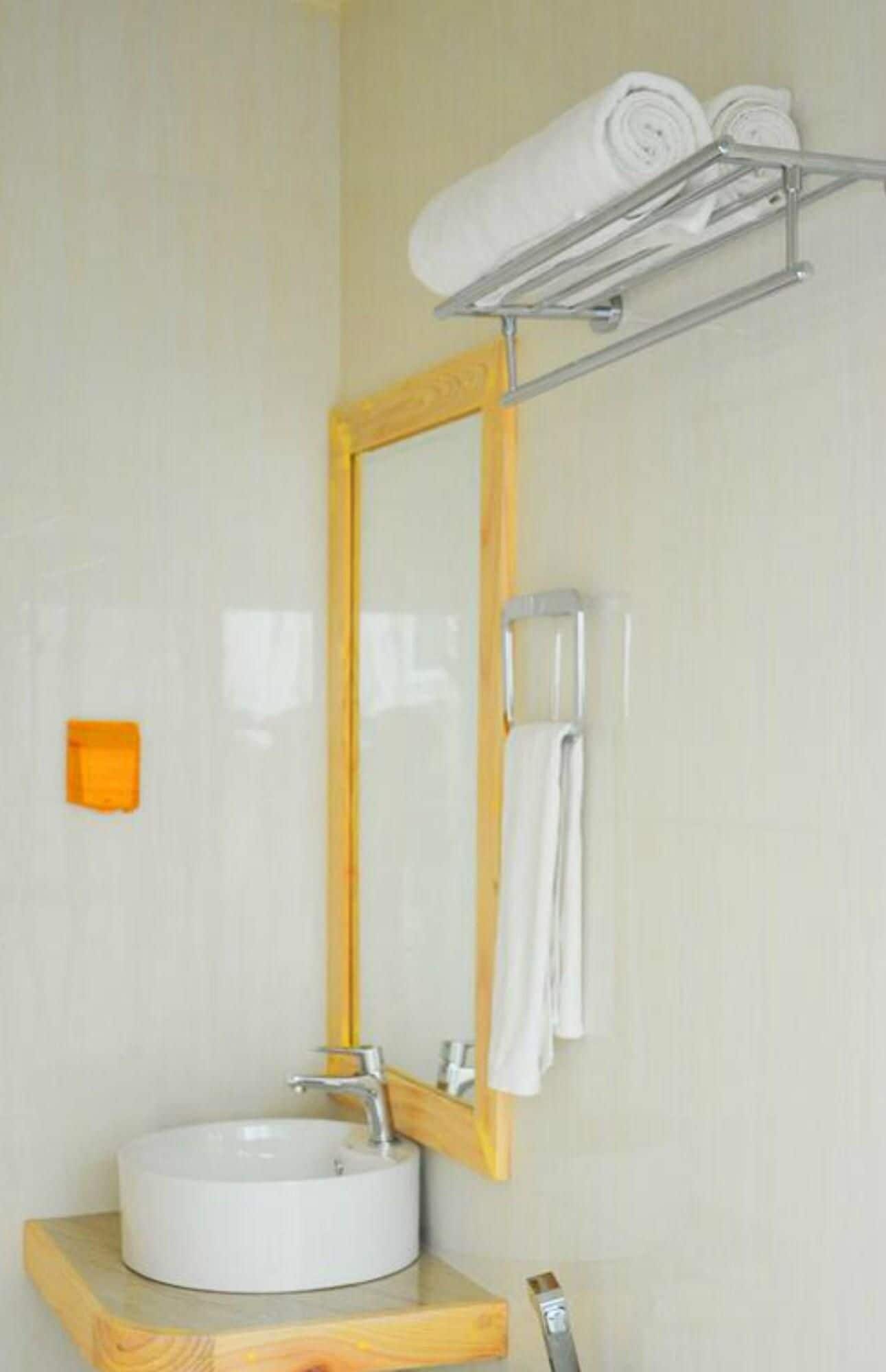 Un baño con un lavabo redondo, un mueble de tocador de madera, un espejo con marco de madera y un perchero con toallas dobladas.