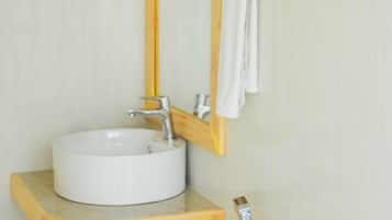 Un baño con un lavabo redondo, un mueble de tocador de madera, un espejo con marco de madera y un perchero con toallas dobladas.
