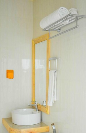 A bathroom with a round sink, a wooden vanity, a mirror with a wooden frame, and a towel rack with folded towels. - Alaka At Maafushi (Maafushi)