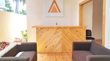 Un área de recepción con un mostrador de madera con motivo de espiga, dos sillones grises y un logotipo montado en la pared.
