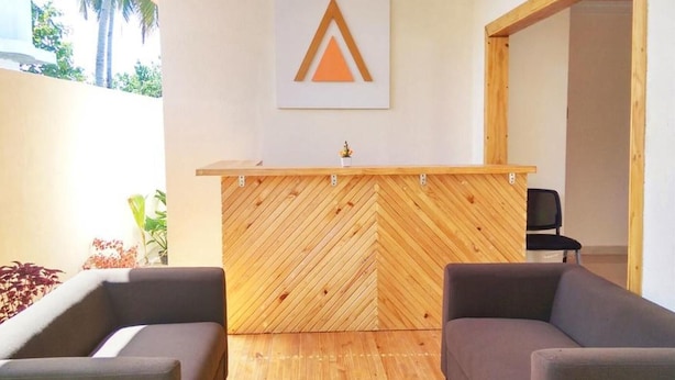 Ein Empfangsbereich mit einem Holzbüro im Fischgrätmuster, zwei grauen Sesseln und einem an der Wand befestigten Logo.