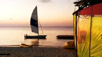 Escena de playa con un velero y una tienda de campaña.
