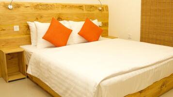 Una cama con ropa blanca y dos almohadas naranjas, un cabecero de madera y una mesita de noche con una lámpara.