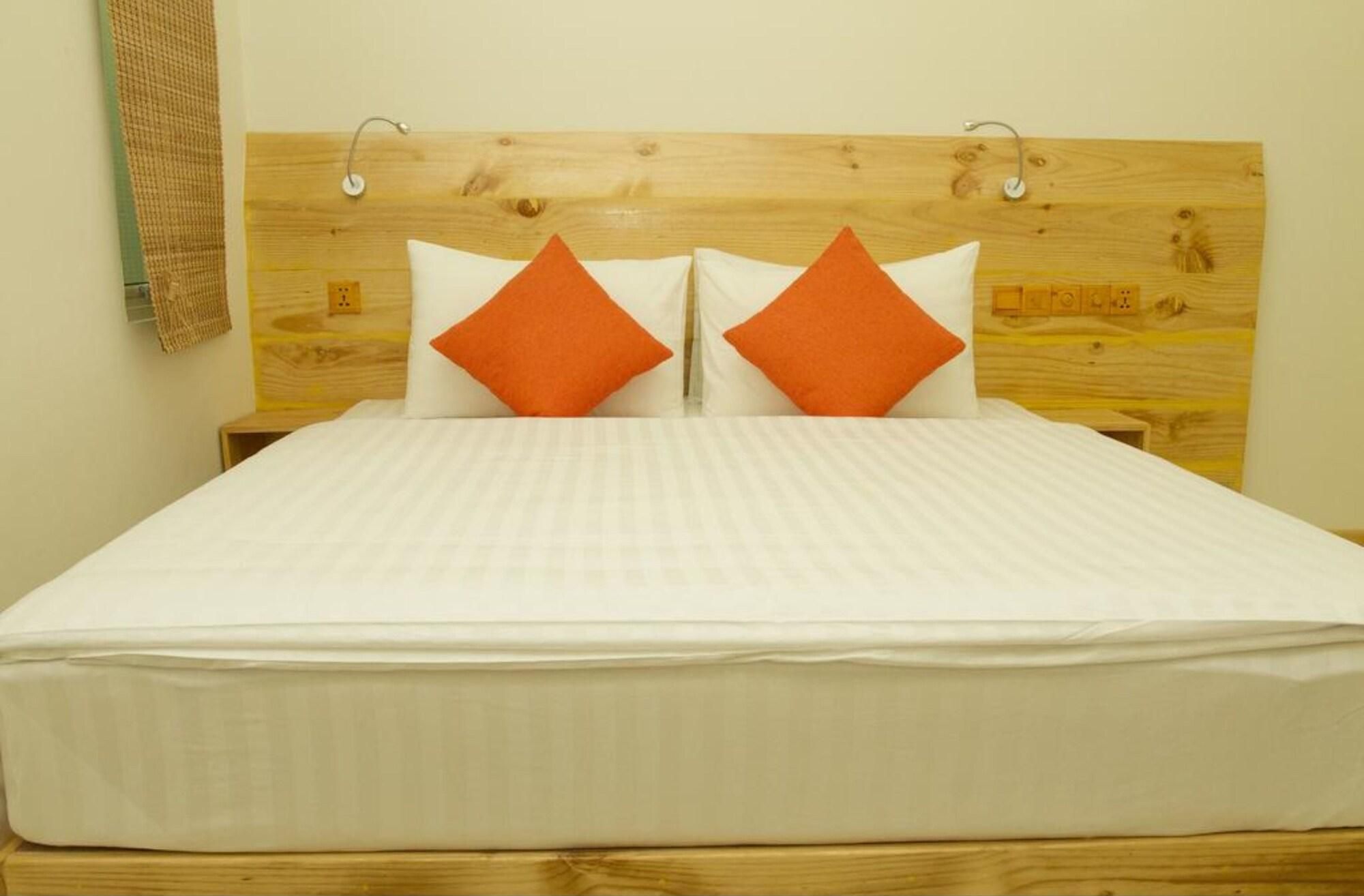 Una cama con cabecera de madera, ropa de cama blanca y dos almohadas naranjas.