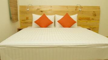 Una cama con cabecera de madera, ropa de cama blanca y dos almohadas naranjas.